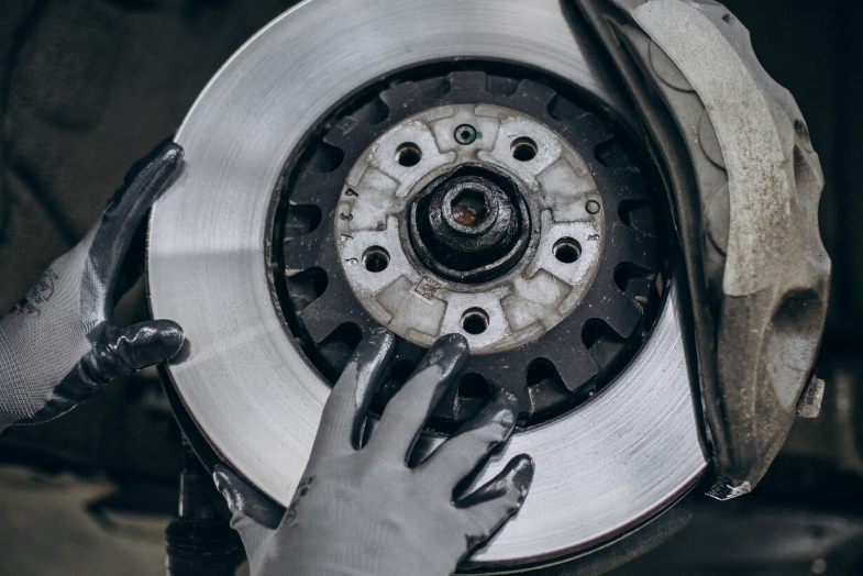 Gloved hands inspecting a brake rotor and caliper