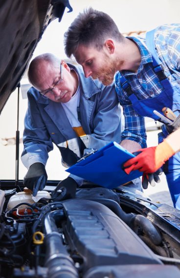 Two mechanics reviewing a checklist over an open hood